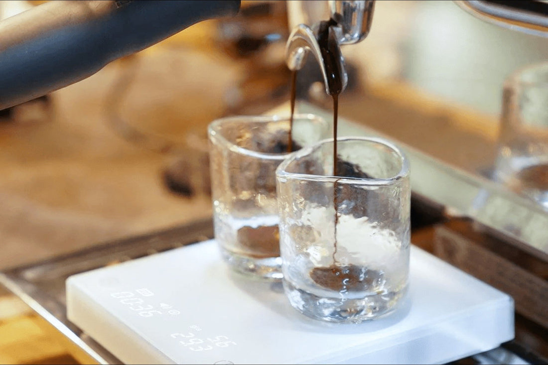 Un portafiltro doppio che estrae in due bicchierini di vetro appoggiati sulla bilancia, con il caffe' che scende dai due becchi
