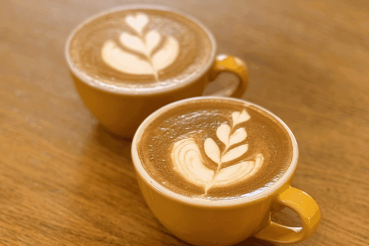 Due cappuccini in tazze gialle con la rosetta disegnata nella schiuma, sul piano di legno chiaro