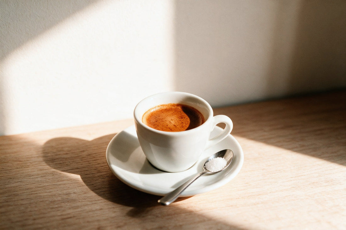 Un espresso in tazzina bianca con la crema intera, e sul piattino il cucchiaino con una dose di zucchero