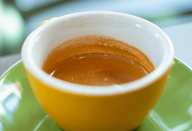 Espresso servito in una tazzina gialla su piattino verde presso CoffeeStorming.